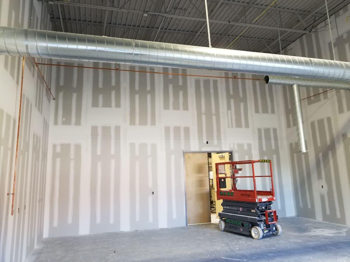 Tall commercial walls taped and coated, with a scissor lift and exposed ductwork