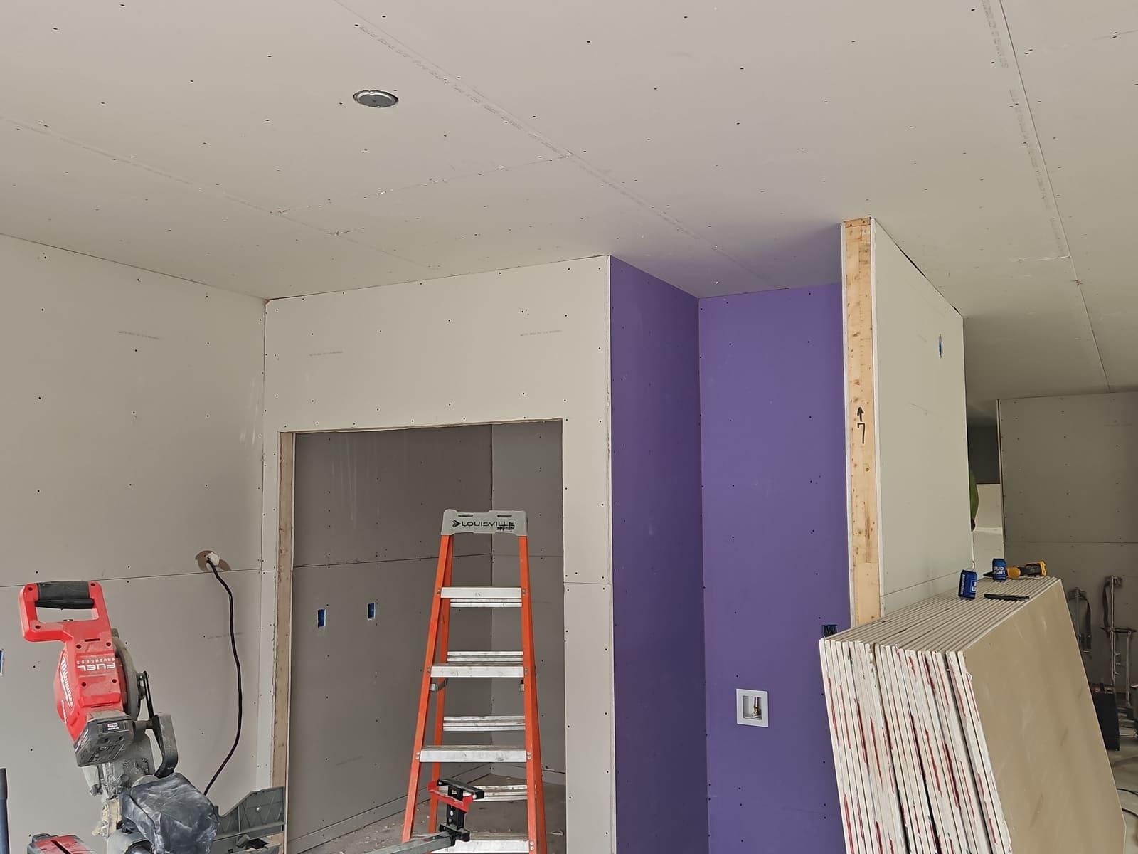 Freshly hung drywall walls and ceiling with purple moisture-resistant board around a closet